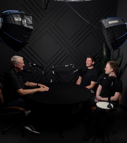 Three people talking around a table in a podcast recording studio